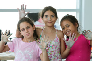 image of three girls smiling and waving during art camp