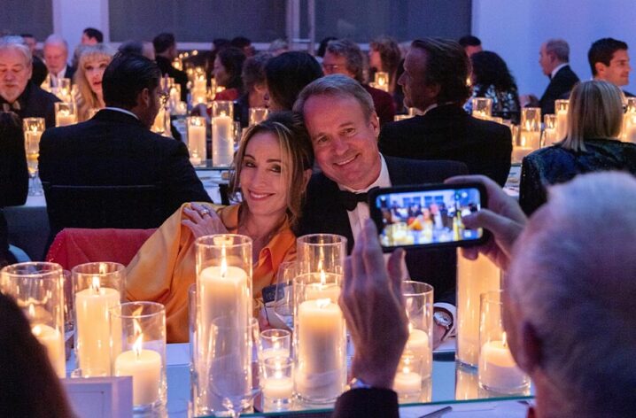Two guests having their photo taken by a friend at a seated gala dinner surrounded by elegant candles.
